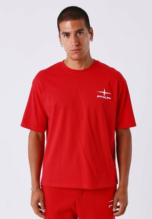 Camiseta roja de manga corta fabricada en algodón con un corte relajado. Presenta un logo blanco en la parte izquierda del pecho y una textura suave.