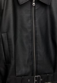 Schwarze Lederjacke mit Reißverschluss vorne, Kragen, Seitentaschen und tailliertem Gürtel mit Metall-Schnalle. Strukturierte, glatte Oberfläche.