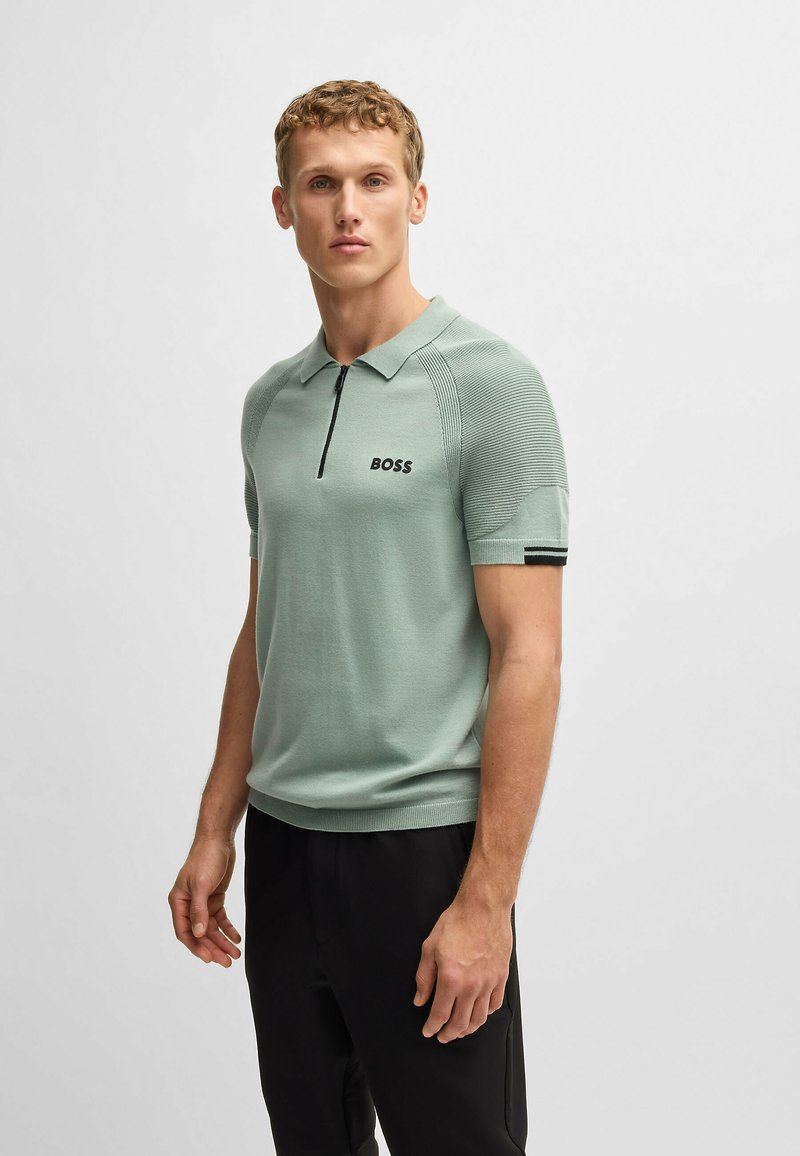 Green knitted polo shirt with a zip collar, featuring a subtle textured pattern and the brand "BOSS" embroidered in black on the chest.