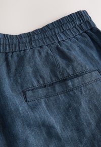 Dark blue denim shorts with an elastic waistband, featuring a back pocket and a textured fabric. Minimalistic design with subtle stitching details.