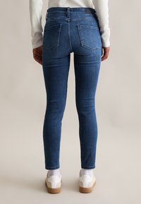 Ciemnoniebieskie rurki o gładkim wykończeniu, z dwiema tylnymi kieszeniami i średnim stanem, zestawione z białymi trampkami i skarpetkami do kostek.