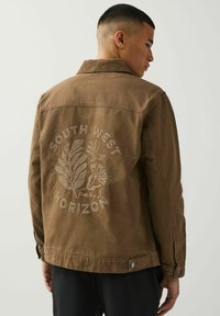 Bruine denimjack met een geborduurd ontwerp op de rug met "SOUTH WEST HORIZON" en bloemaccenten. Gestructureerde kraag en knopen.