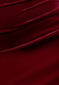 Tissu en velours rouge profond avec une texture lisse et un drapé doux. La surface présente un léger brillant et des plis ondulants. Aucun motif.