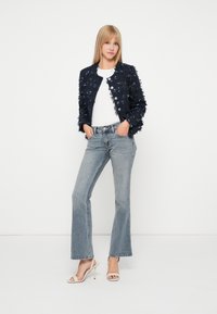 Jūras spēku teksturēta jaka ar saplēstām malām, apaļu kakla izgriezumu un pogām. Apvienota ar gaismas zilām zvanu biksēm un bēšām siksniņu kurpēm.