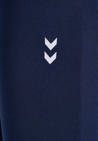 Marina atletiska leggings med strukturerad tyg, vertikal ribbning och vit chevron-logotypdetalj nära sidan.