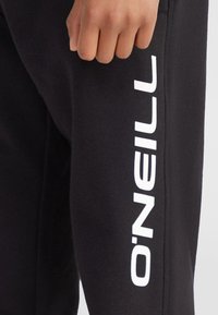 Čierne jogger nohavice vyrobené z mäkkej látky, s výrazným bielym logom "O'Neill" pozdĺž strany a priliehavým strihom.