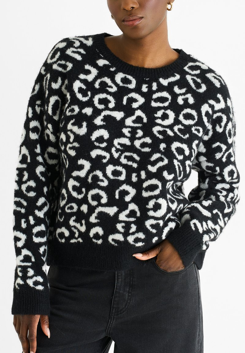 Schwarzer Pullover mit einem flauschigen weißen Leopardenmuster, Rundhalsausschnitt und gerippten Bündchen, kombiniert mit dunklen Jeans.