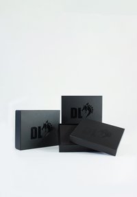 Boîtes d'emballage en papier noir avec une finition mate, ornées d'un logo en relief représentant un cheval et les lettres "DL", disposées en formation décalée.