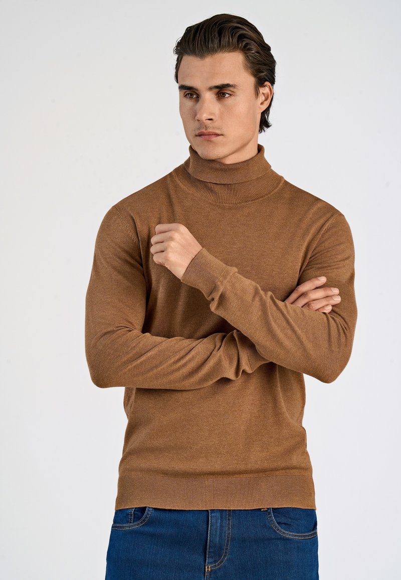 Maglione dolcevita color bronzo realizzato in tessuto morbido, con maniche lunghe e polsini a coste, abbinato a jeans blu scuro.