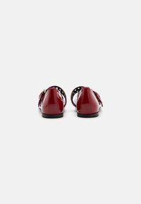 Rote Lackleder-Ballerinas mit einem Rückendesign, das Fransenakzente und Ausschnitte aufweist. Schwarze Sohle, glatte Textur und runde Zehenform.