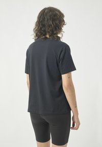 Schwarzes Baumwoll-T-Shirt mit kurzen Ärmeln, lockerer Passform und Rundhalsausschnitt, kombiniert mit schwarzen, figurbetonten Shorts.