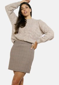 Light beige knitted sweater with a textured design, paired with a fitted brown and tan houndstooth skirt, showcasing a smooth finish.