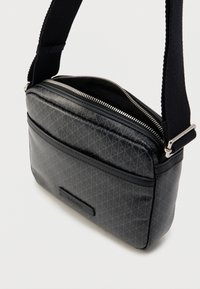 Μαύρο συνθετικό τσαντάκι χιαστί με γεωμετρικό μοτίβο. Διαθέτει κλείσιμο με φερμουάρ, ρυθμιζόμενο λουράκι και μπροστινή τσέπη. Υφή με ανάγλυφο μοτίβο.