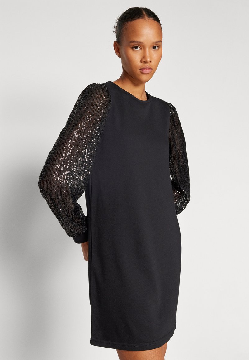 Robe noire avec de longues manches bouffantes pailletées. Le tissu principal est lisse et ajusté, tandis que les manches présentent un motif texturé et scintillant.