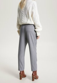 Kabelbrei crème trui en grijs houndstooth-patroon broek, met een taps toelopende pasvorm en bruine haklaarzen.