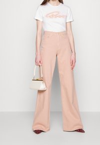 Light pink wide-leg jeans paired with a white T-shirt featuring colorful text. A small, structured white handbag is held in one hand.
