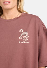 Vihreä puuvillapaita rentoa mallia, jossa on valkoinen grafiikka hymyilevästä aallosta ja auringosta, sekä teksti "BILLABONG."