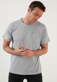 Világosszürke, rövid ujjú póló kerek nyakkivágással, bal oldali mellkason texturált zsebfedéllel és sima anyaggal.