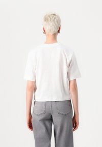 Hvit cropped t-skjorte laget av bomull, med korte ermer og rund hals. Grå høytlivsjeans med baklommer og synlige sømmer.