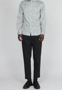 Vit långärmad skjorta med liten grön blommönster, knäppt, kombinerad med svarta snäva byxor och svarta snörskor.