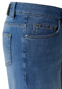 Blue denim jeans feature a mid-rise design, yellow stitching, a patch pocket, and a branded tag on the back waistband.