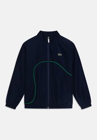 Námořnická větrovka vyrobená z lehké tkaniny, s designem zelené zakřivené linie, vysokým límcem a zipovým zapínáním. Malé logo na hrudi.
