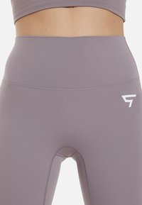 Lilla højttalede leggings lavet af et glat, strækbart stof. Har et lille hvidt logo på hoften og forstærkede syninger.