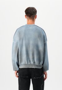 Sweatshirt oversized cinza-azulado com uma textura suave, de gola redonda e três botões nas costas, combinado com jeans pretos texturizados.