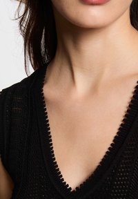 Top in maglia nera con scollatura a V e bordo ondulato, motivo testurizzato e vestibilità rilassata, realizzato in un mix di materiali morbidi e traspiranti.