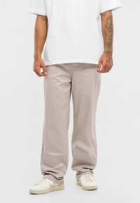 Svetlobéžové nohavice z hladkej tkaniny, ktoré majú uvoľnený strih a minimalistický dizajn. Skombinované s bielymi teniskami.