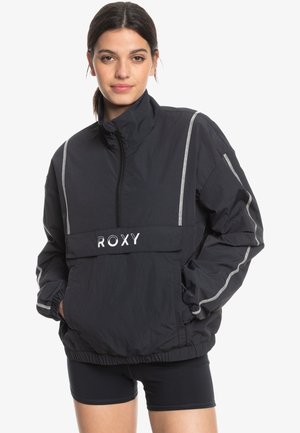 Black windbreaker jacket featuring a high collar, front pocket, and white logo. It has reflective side stripes and an elastic hem.