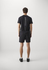 Čierne atletické tričko s krátkymi rukávmi a potlačou loga na chrbte, kombinované s vhodnými čiernymi šortkami a športovou obuvou.