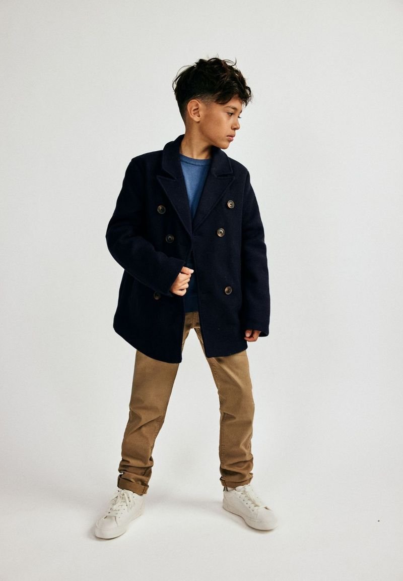 Tumesinine kahekordne jope, mis on valmistatud villasegusest, suurte nööpidega, kantud sinise särgi peal, koos bee�žide pükste ja valgete tossudega.