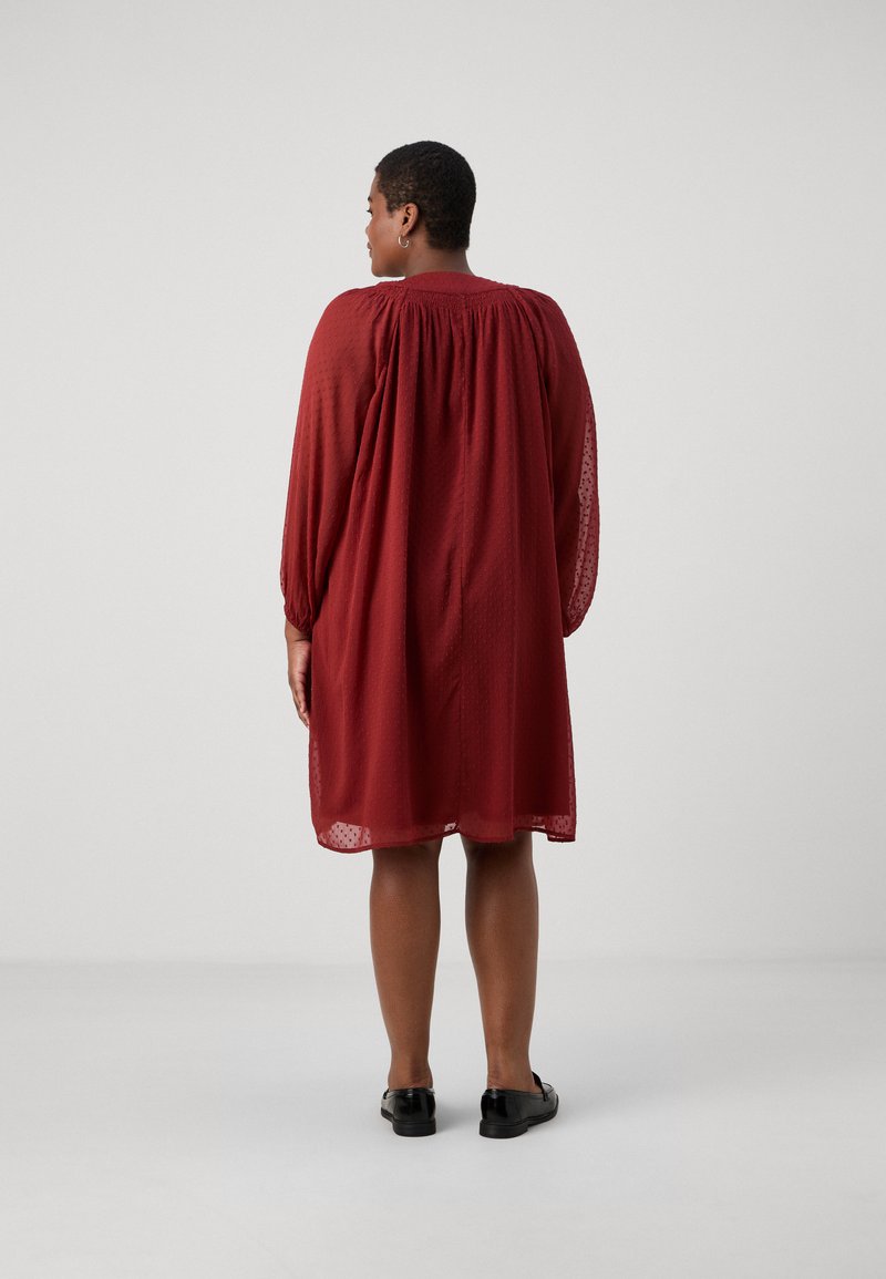 Rotes knielanges Kleid mit lockerem Schnitt, langen Puffärmeln und einem strukturierten Stoffmuster. Glatter Rücken und geraffte Ausschnittdetails.