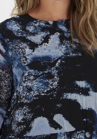 Tejido negro con un patrón abstracto azul; textura suave, escote redondo, mangas largas y detalle fruncido en la cintura.