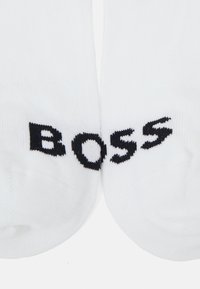 Biele ponožky vyrobené z bavlnenej zmesi s výrazne vyrazeným čiernym logom "BOSS" na každom prste. Hladká textúra s ribovaným dizajnovým detailom.