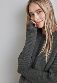 Maglione grigio a coste con maniche lunghe, tessuto testurizzato e vestibilità morbida. La visione ravvicinata mostra il materiale morbido e il dettaglio casual delle maniche.