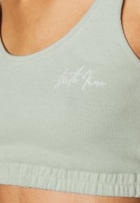 Camisola curta em verde claro com textura canelada e decote redondo, apresentando um logótipo bordado na parte inferior e uma bainha elástica para um ajuste confortável.