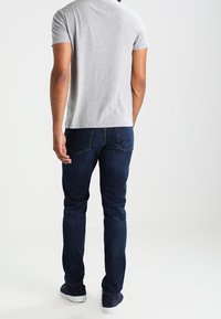 Camiseta de hombre de manga corta gris y jeans ajustados de color azul oscuro. La camiseta tiene un diseño liso; los jeans presentan bolsillos traseros y un color sólido.