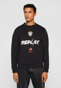 Black sweatshirt, cotton blend, crew neck, featuring a large white "REPLAY" print, logo with stripes, and a badge with three stars.