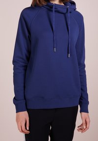 Felpa con cappuccio di colore blu navy, dalla vestibilità rilassata, con lacci e polsini a costine. Tessuto morbido e senza motivi o dettagli visibili.