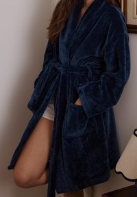 Robe en polaire bleu marine, avec un design enveloppant, des manches larges, deux poches avant et une ceinture assortie. Texture lisse et douce.