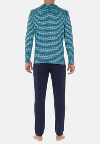 Langärmliges Hemd mit einem blauen geometrischen Muster, kombiniert mit einer navyblauen Hose. Das Hemd hat einen runden Halsausschnitt und schmal geschnittene Ärmel.