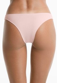 Vrouw in lichte roze geribbelde bikini broekjes, achteraanzicht tegen een plain witte achtergrond.