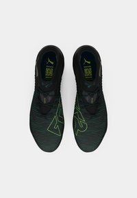 Black athletic shoes with a textured upper, featuring green stripes and a large logo design. Lacing is central, with a padded collar.