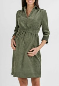 Olijfgroen korduroy jurk met een geklede halslijn, driekwartmouwen en een elastische taille. Zachte textuur met verticale ribbels.
