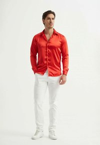 Chemise rouge en satin à manches longues avec un devant boutonné, associée à un jean blanc et des baskets blanches. La chemise a une texture lisse et brillante.
