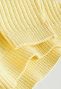 Țesătură ribbed de culoare galben deschis, cu o textură moale, având linii verticale uniforme și margini finisate cu grijă, stratificată pentru adâncime.