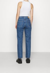 Jeans de mezclilla azul de tiro alto con corte recto, que cuentan con dos bolsillos traseros y una etiqueta de cuero en la cinturilla. Tejido texturizado.