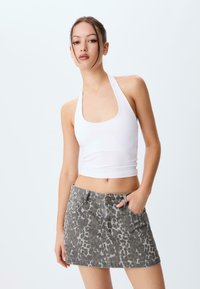 Haut court blanc avec un col halter associé à une mini-jupe en denim gris à imprimé léopard. Présente une silhouette ajustée et des poches avant sur la jupe.